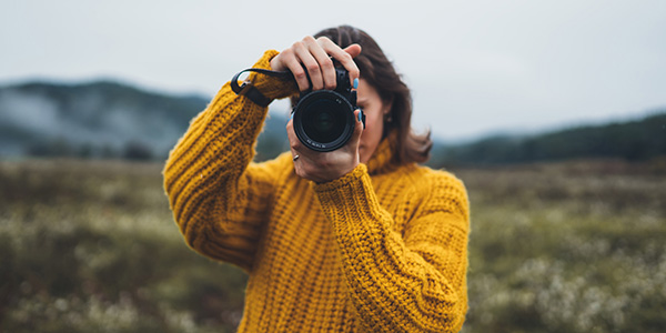 Woman facing camera, taking photo with a camera.